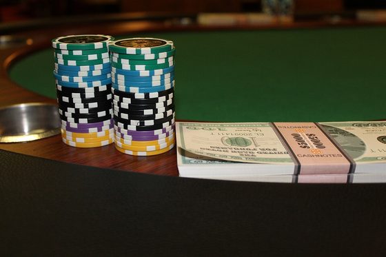 Stacks of poker chips and banded cash on a green felt cash-game table