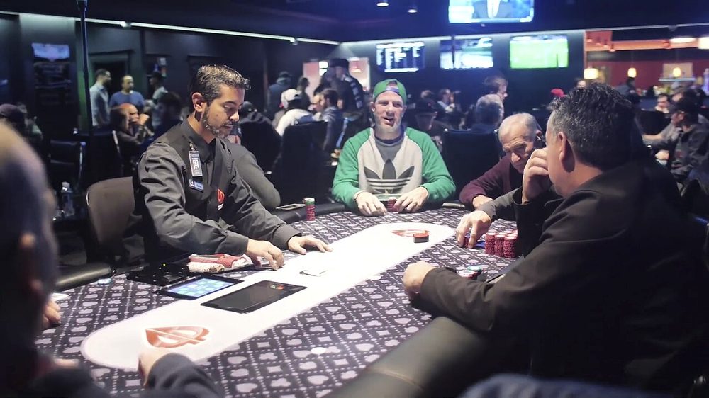 Players and a dealer at a busy live poker table in a card room