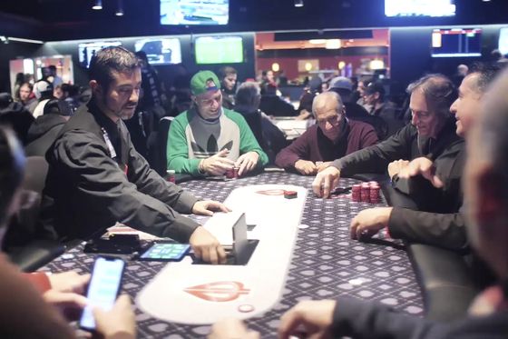 Players seated around a poker table on a busy tournament floor